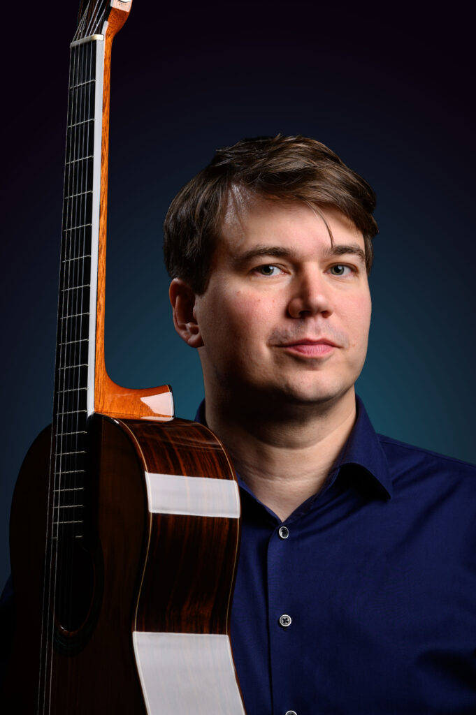 Musiker Patrik Kleemola bredvid en akustisk gitarr.